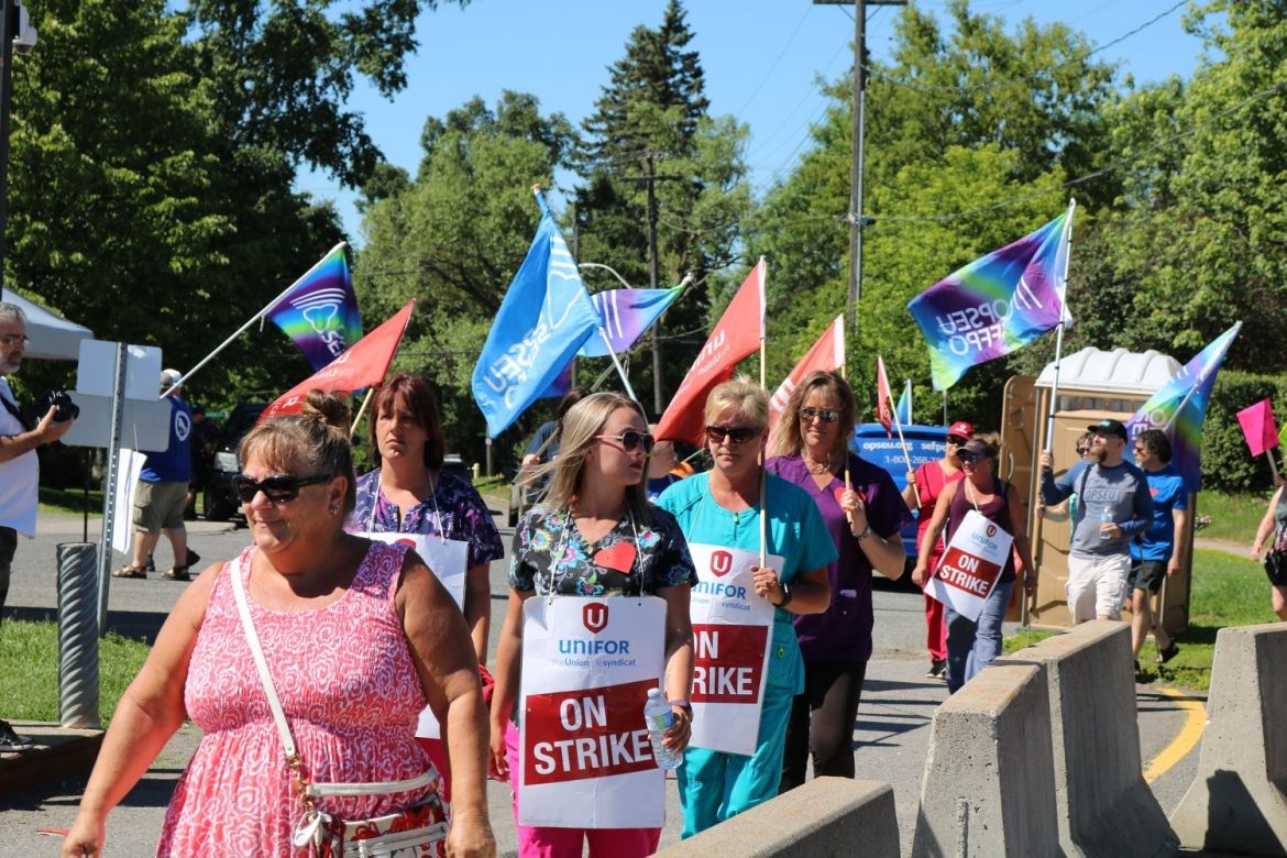 Health care workers walk a picket line while carrying flags for Unifor and OPSEU.