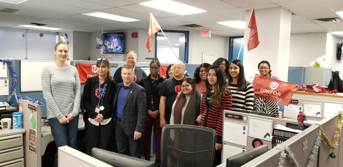 A dozen members of Unifor Local 16-O standing between two rows of cubicles.