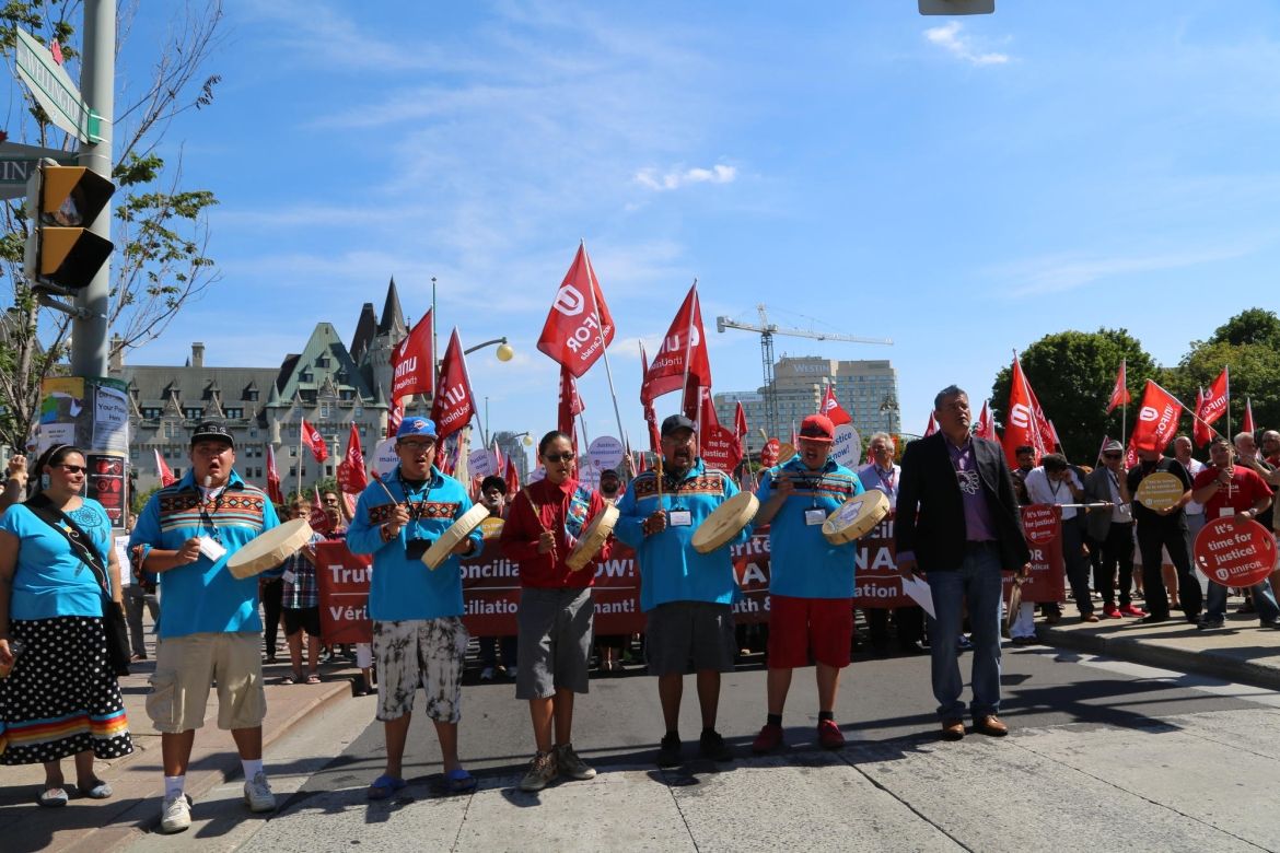 Une rangée de joueurs de tambour indigènes dirige un groupe de militants d'Unifor lors d'un rassemblement.