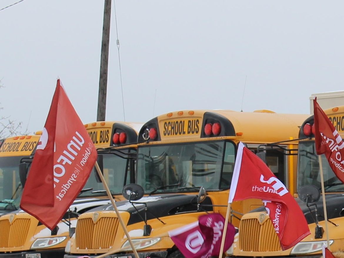 Unifor flags fly in front of a row of school buses.