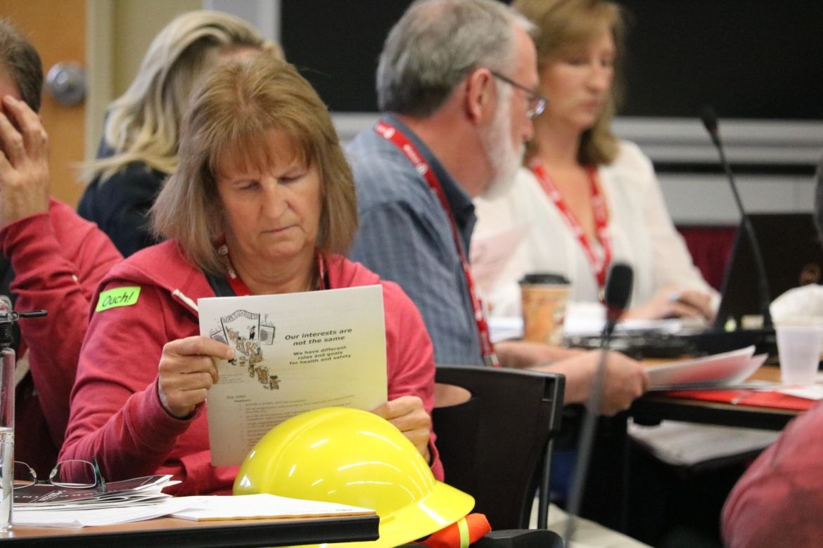 A Unifor member, with a hard hat resting on their knee, sits in a meeting reading a handout.