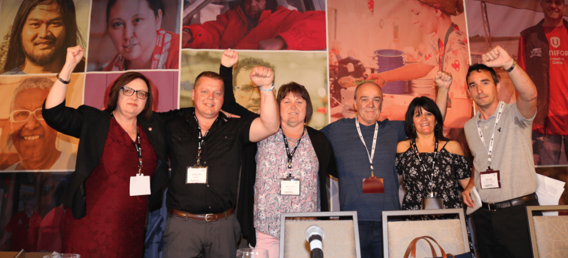 Lana Payne, Shane Wark and members of Unifor Local 597 raise their fists in solidarity from the stage at Atlantic Regional Council.