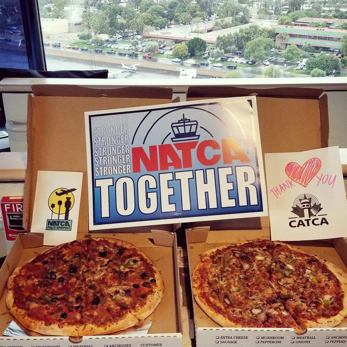 Two pizzas sittign in open boxes with signs reading &quot;NATCA Stronger Together&quot; and &quot;Thank you CATCA.&quot;