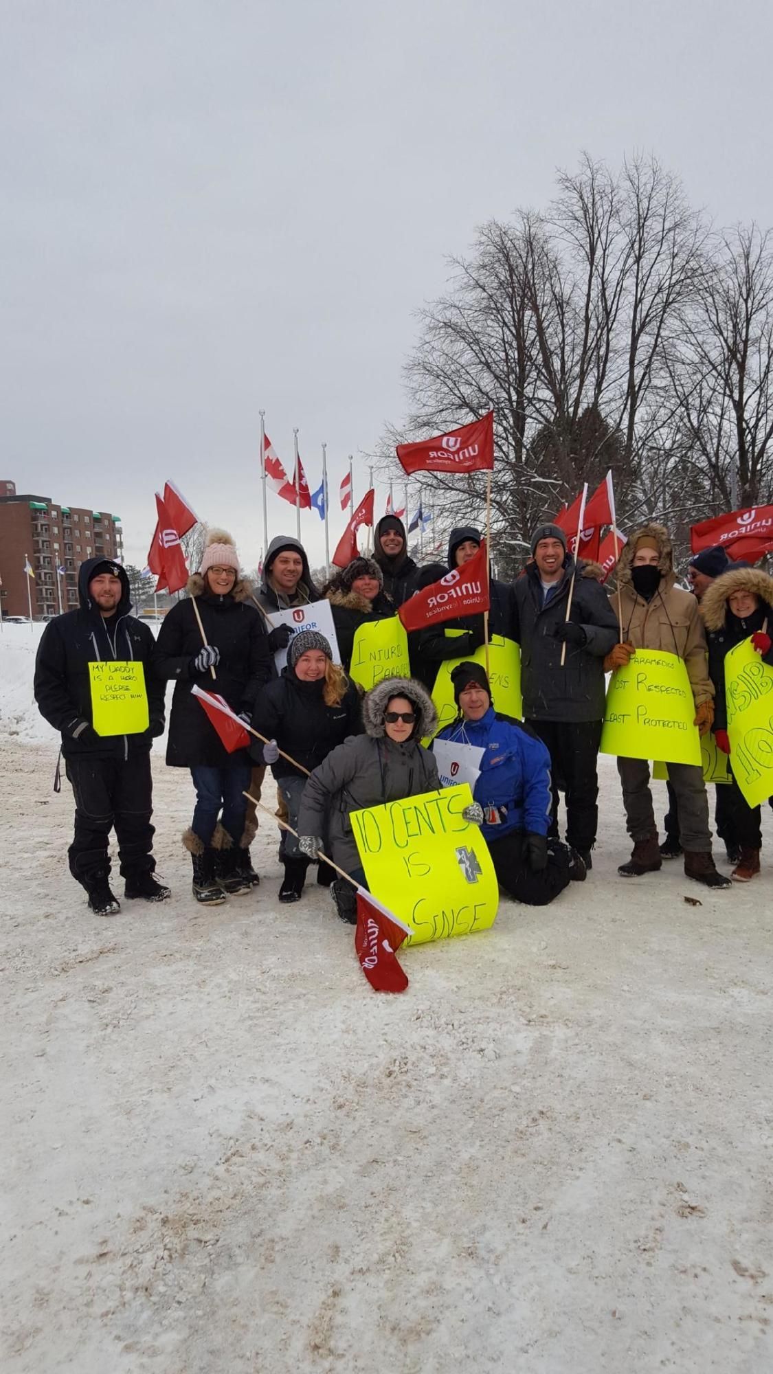 A dozen Local 1359 members, in cold weather gear, carry flags and signs.