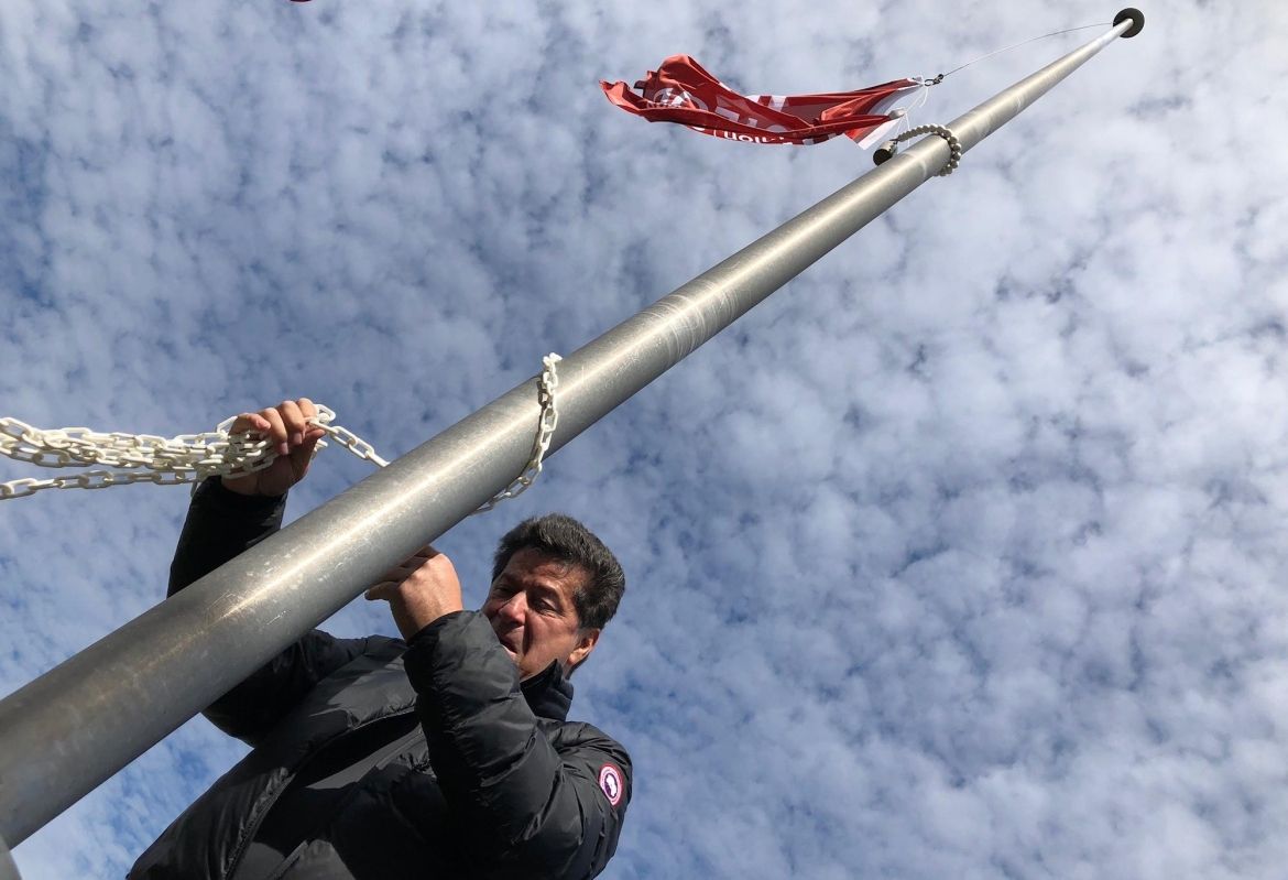 Jerry Dias, visiblement ému, abaisse le drapeau d'Unifor devant un ciel couvert de nuages.