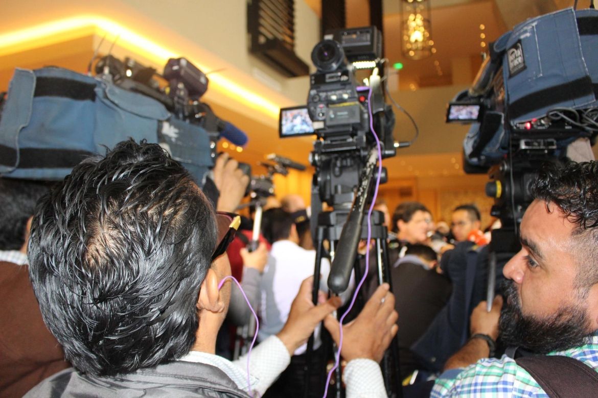 Two videographers hold their cameras steady during a press conference.