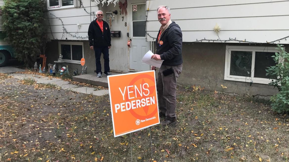 Un panneau de campagne pour Yens Pendersen est vu sur la pelouse d'une maison où deux membres d'Unifor font du porte-à-porte.