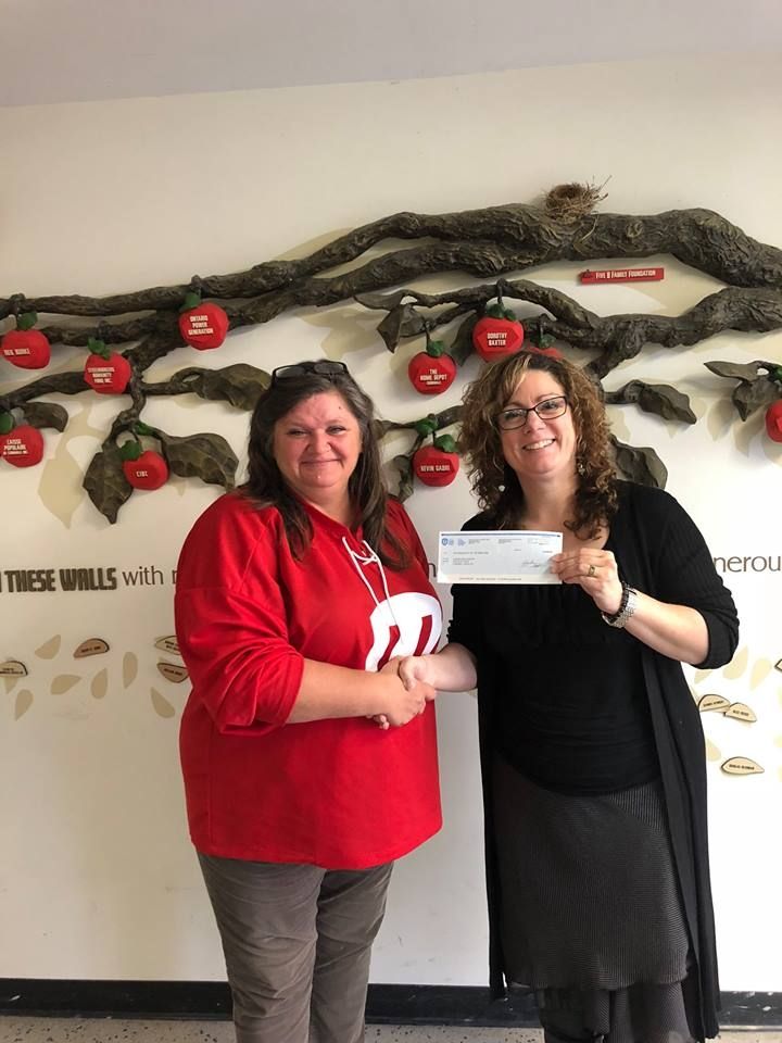 A Unifor member wearing a red Unifor jersey presents a donation cheque.