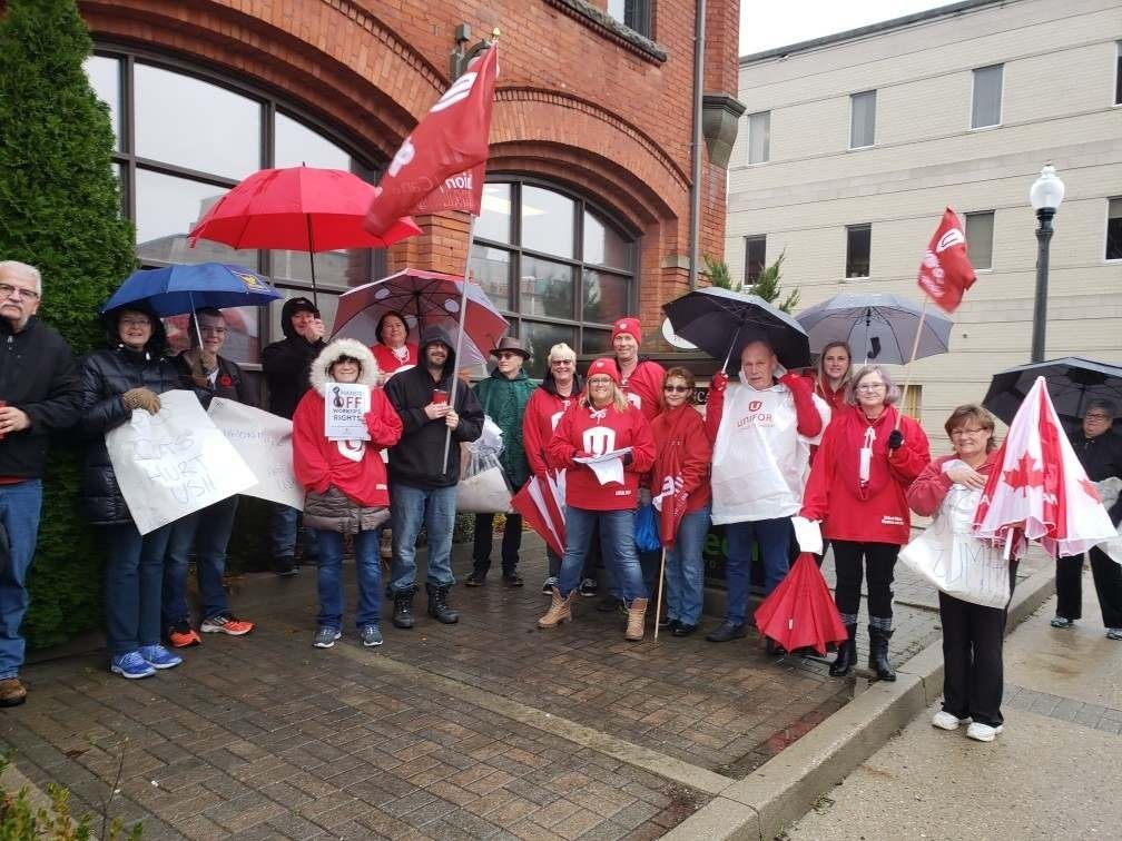 Unifor members wearing matching red shirts as they huddle under umbrellas.