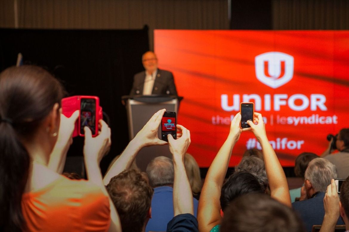 A crowd of people holding up their phones to camera photos and video at a Unifor event