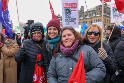 Four women outside in winter gear holding red flags smiling