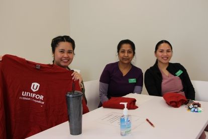 A small group of long term care workers smile brightly while holding Unifor t-shirts.