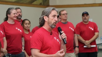 A man at a microphone with people standing behind him