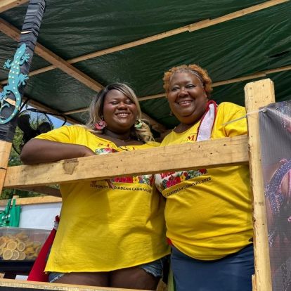 Two people wearing yellow shirts leaning on a fence smiling