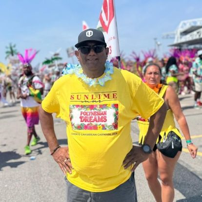 A man posing in front of carnival attendees wearing a sunlime tshirt