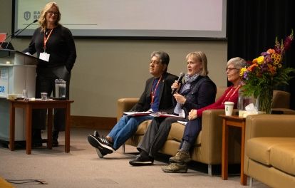 Three people sitting on chairs, one is speaking into a mic