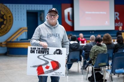 A man holds a sign that reads; Slam the breaks on tariffs