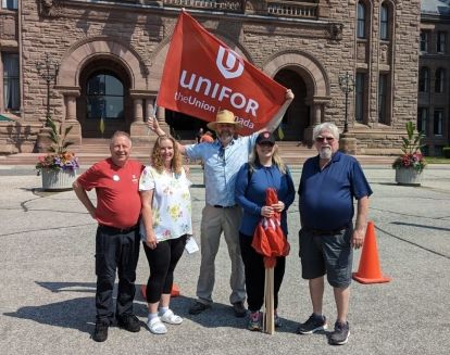Five people standing in front of Queen's Park holding a Unifor flag