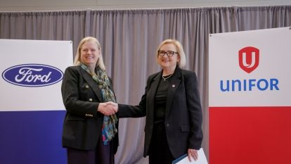 Two women shaking hands between a Ford and Unifor x-stand banners