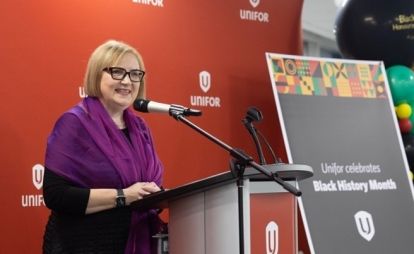 A women speaking at a podium standing beside a banner.