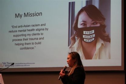 A women speaks into a mic in front of a presentaion screen