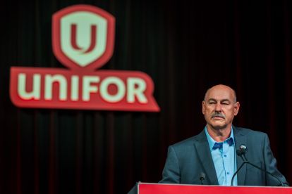 A man at a podium Unifor shield sign on a black background