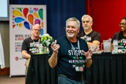 Three men stadning at the front of a room one is talking through a headset