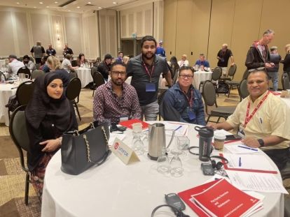 Five people at a table, four of them seated and posing for a photo.