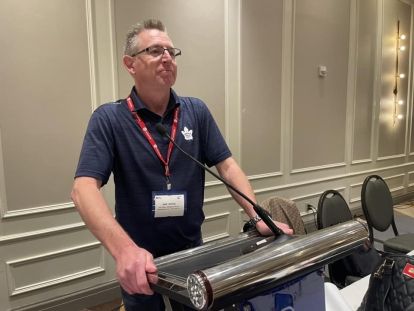 A man in a blue Maple Leafs polo shirt stands at the podium.