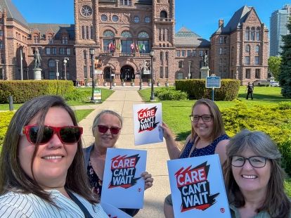 Four women outside parliment hill on a sunny day holding placards that read, Care Can't Wait.