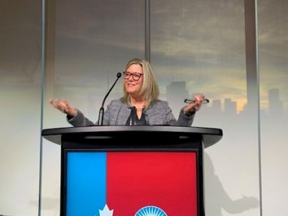 A woman speaks at a blue and red podium.