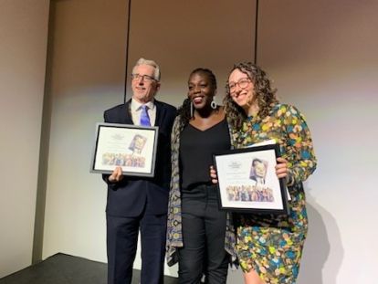 A man and woman holding award plaques with a woman standing in the middle.