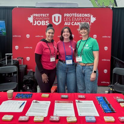Three Unifor members stand behind a table with factsheets and in front of a backdrop reading 'Protect Canadina Jobs'