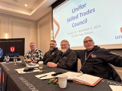 Four people sitting at a table in front of a presentation screen