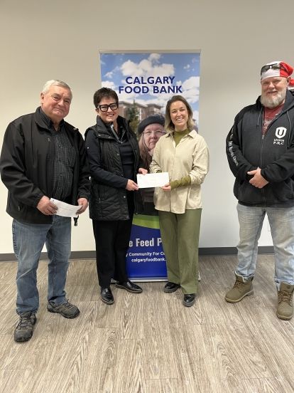 Four people holding a cheque in front of a xstand banner