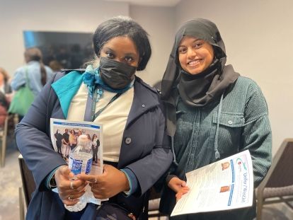 wo women, one wearing a face mask and a turquoise WestJet uniform, smile for the camera while holding a Unifor brochure.