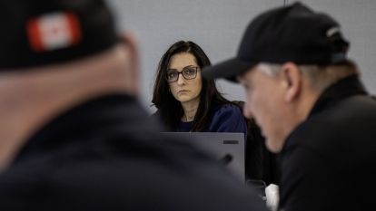 Katrina Peterson looks on with two men in the foreground.