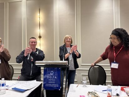 Two women and a man stand behind a podium clapping