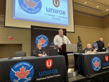 A man speaks at a podium a man sits at each side