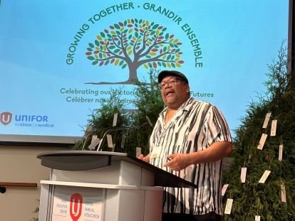 Derek Barry speaking at a podium in front of a presentation screen