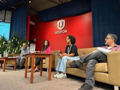 A panel of four on stage sitting on couches. A screen inbehind red with a white Unifor logo.