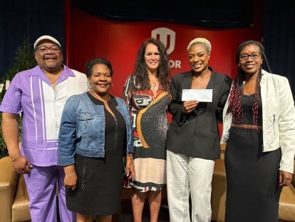 Five black people standing toghter one is holding up a cheque.