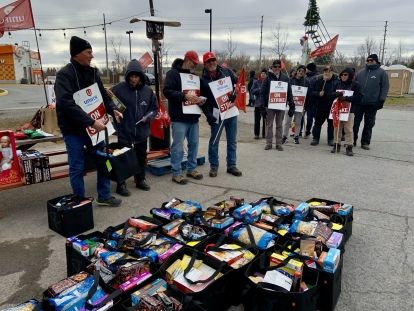 Striking workers wearing &quot;on strike&quot; signs stand outside, gift bags line the ground.