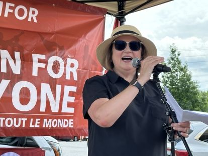 women speaking with microphone with unfor for one sign in background