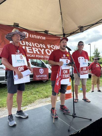 3 people in red shirts on stage with unifor union for everyone in the background