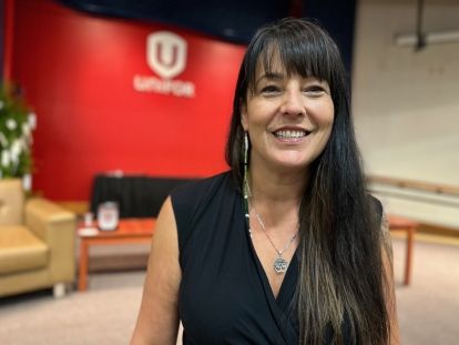 A women smiling at the camera infront of a Unifor screen.