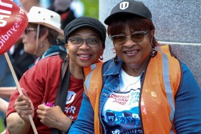 Two Uniformed members smile while at rally and holding red Unifor flags.