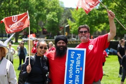 Unifor Ontario Regional Director Samia Hashi poses for photo with two Uniformed leaders wearing red and waving Uniformed flags.