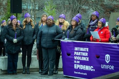 A group of women wearing purple beenies and holding a banner
