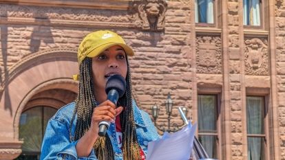 A women speaks into a mic in front of Queen's Park